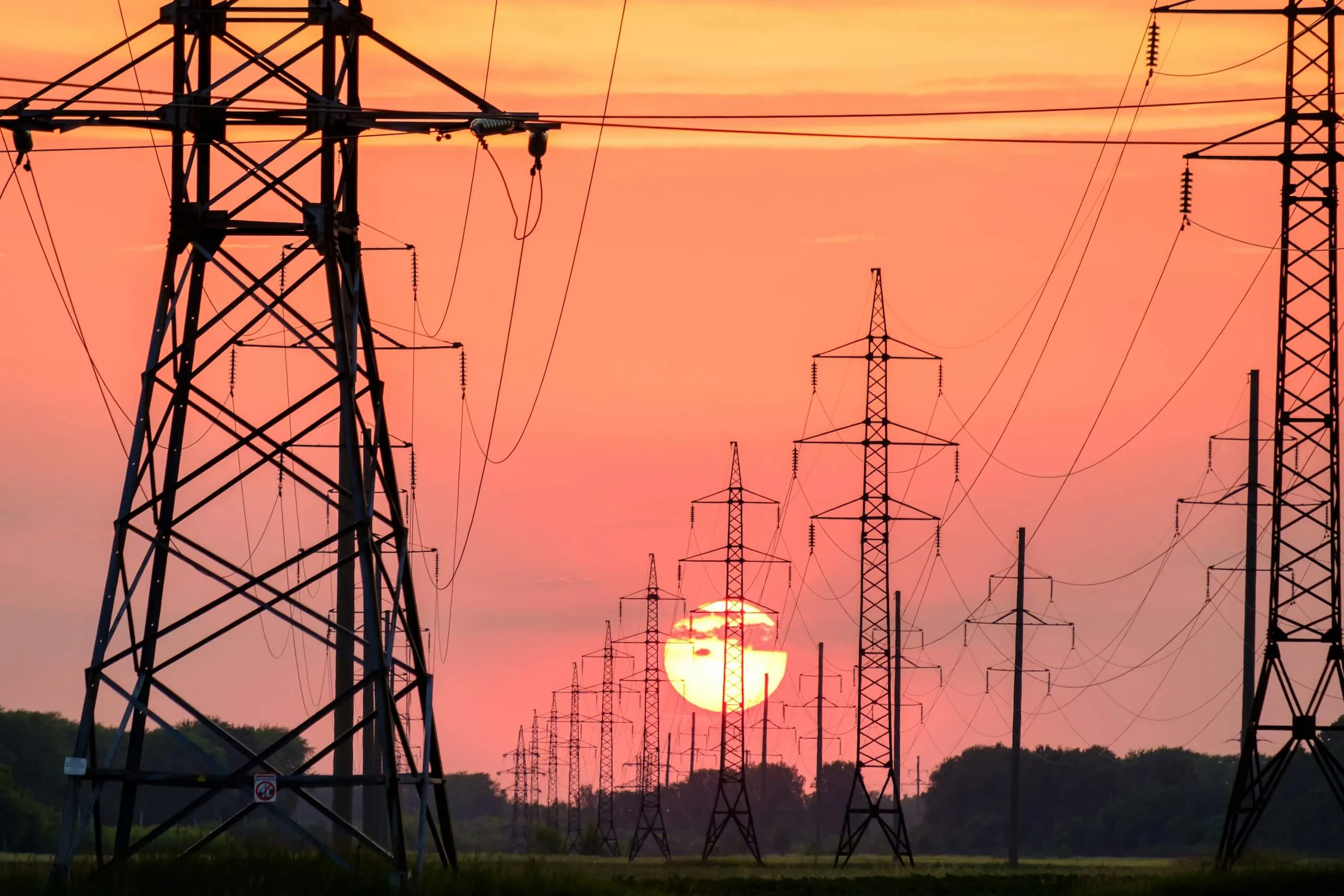 Electricity pylons and power lines silhouetted against a sunset