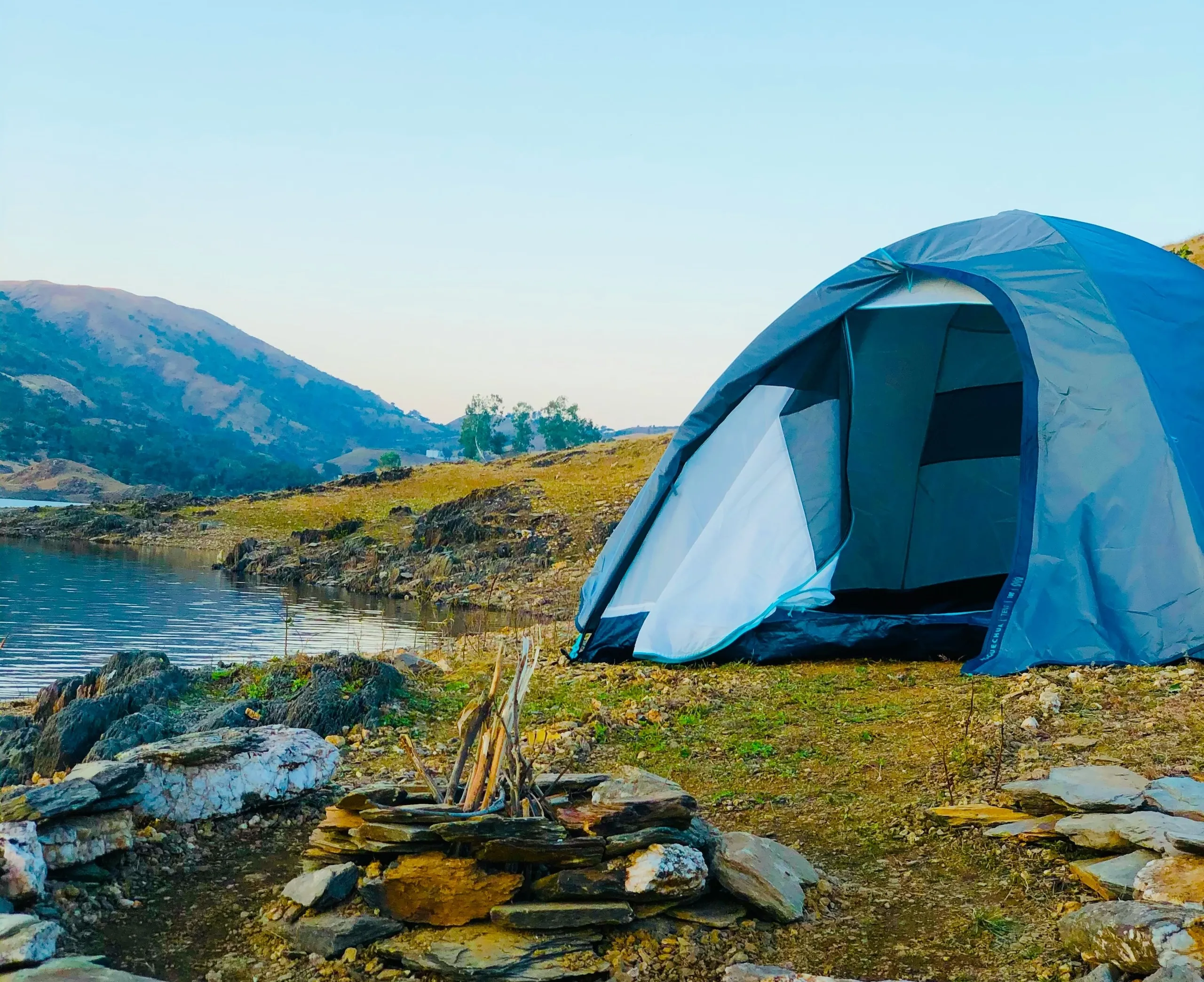 A white dome tent on a green grass field beside a body of water