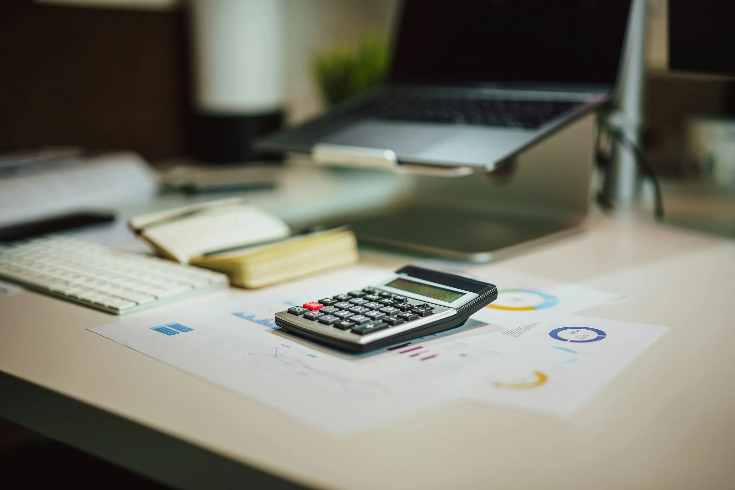 A calculator on printed financial charts beside a laptop on a desk