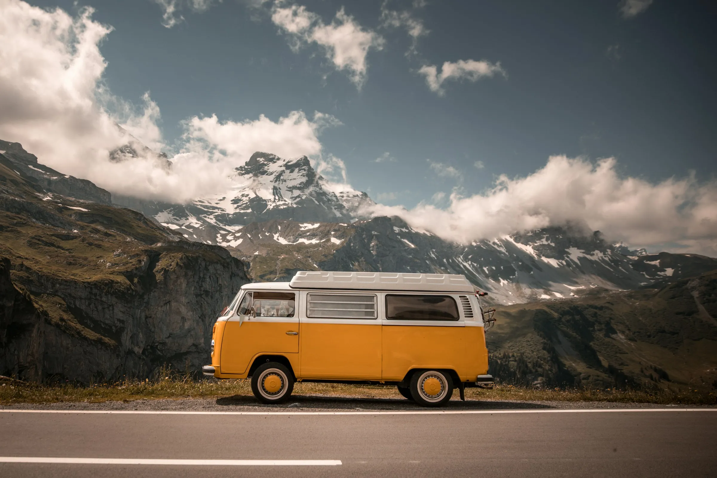 An orange and white campervan parked beside a mountain road